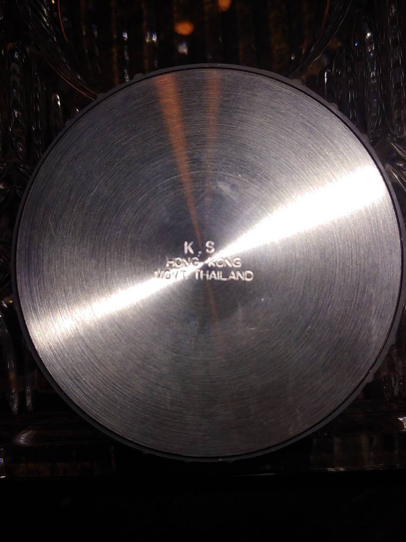 May include: A silver-colored metal disc with the text "K.S. HONG KONG MFG. THAILAND" engraved on the surface.