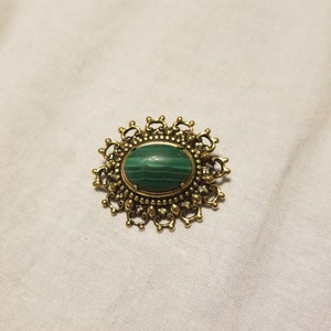 May include: A gold-toned brooch with a green malachite stone set in a detailed, ornate design.