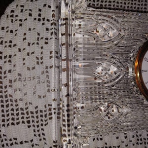 May include: A clear crystal clock with a gold-toned face and black hands. The clock face reads "White Crystal".