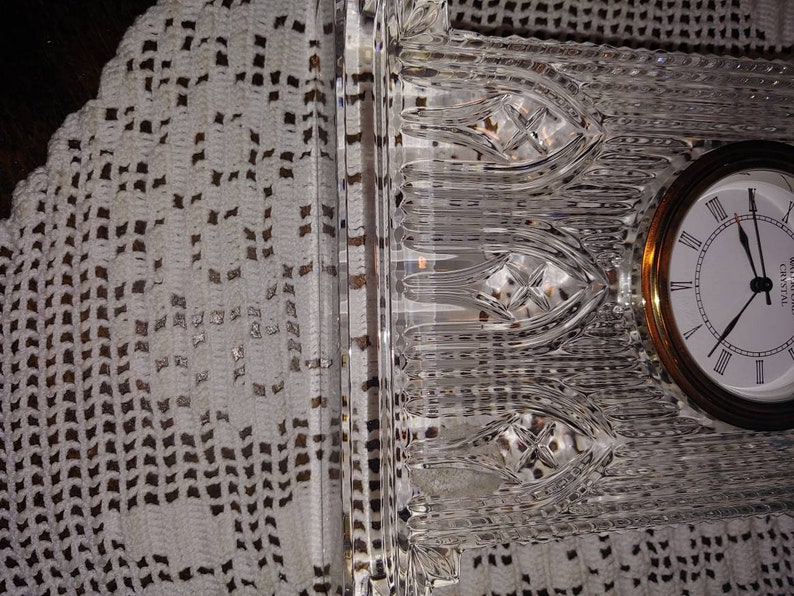 May include: A clear crystal clock with a gold-toned face and black hands. The clock face reads "White Crystal".