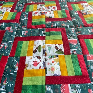 May include: A red, green, and yellow patchwork quilt with a gnome theme. The quilt is made of squares and rectangles of different sizes and colors. The quilt is decorated with gnomes, mushrooms, and other woodland creatures.