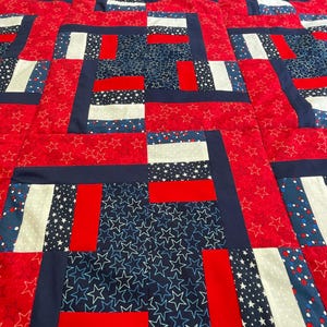 Könnte beinhalten: Ein Patchwork-Quilt mit patriotischem Thema. Das Quiltmuster wiederholt Blöcke aus rotem, weißem und blauem Stoff. Roter Stoff mit weißen Sternen, blauer Stoff mit weißen Sternen. Der Quilt ist mit dunkelblauem Stoff eingefasst.