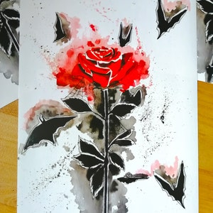 Puede incluir: Una pintura de acuarela de una rosa roja con murci&eacute;lagos negros volando a su alrededor. La rosa est&aacute; rodeada de una lavada de acuarela roja y rosa.