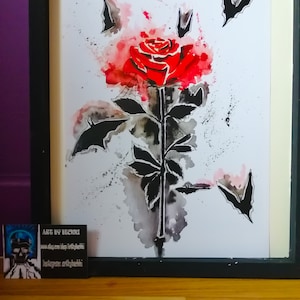 Puede incluir: Una pintura de acuarela de una rosa roja con murci&eacute;lagos negros volando a su alrededor. La rosa est&aacute; pintada en un estilo realista, con un tallo y hojas detalladas. Los murci&eacute;lagos son estilizados y tienen un toque caprichoso. La pintura est&aacute; sobre un fondo blanco.