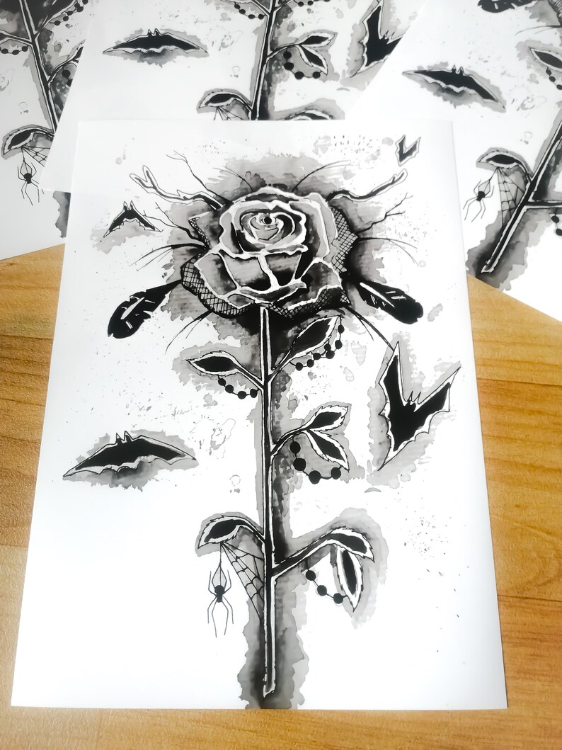 May include: A black and white ink drawing of a rose with a spider web, bats, and beads on the stem. The rose is drawn in a gothic style.