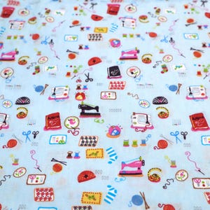 May include: A light blue fabric with a repeating pattern of sewing-themed illustrations. The pattern includes sewing machines, spools of thread, scissors, buttons, needles, and other sewing supplies.