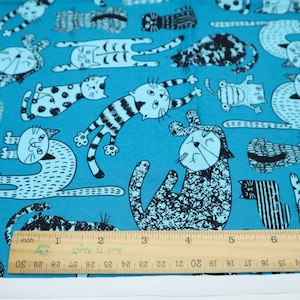 May include: Blue fabric with a repeating pattern of black and white cats in various poses. The fabric is measured with a ruler in inches.