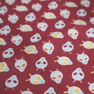 May include: A maroon fabric with a repeating pattern of light blue alien heads with yellow eyes. The aliens have two small antennas on top of their heads.