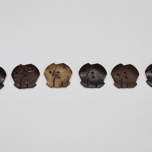 Könnte beinhalten: Sechs braune Kokosnuss-Knöpfe mit einem geschnitzten Elefanten-Design. Die Knöpfe haben jeweils zwei Löcher.
