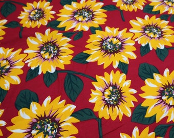 Peut inclure: Tissu rouge avec un motif répétitif de tournesols jaunes. Les tournesols ont un centre blanc avec un centre brun et rose.