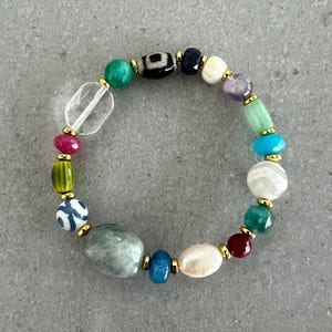 May include: A colorful beaded bracelet featuring a variety of gemstones and beads in shades of green, blue, red, white, and purple. The bracelet includes a clear quartz bead and gold-colored accents.