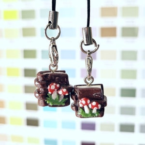 May include: Two brown and white charm pendants with mushroom and leaf details. The charms are attached to black cords with silver clasps.