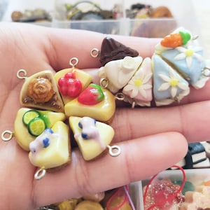 Puede incluir: Una colección de nueve colgantes de comida en miniatura, cada uno con un postre diferente, incluyendo una rebanada de pastel, un cupcake, una galleta y una porción de pastel. Los colgantes están hechos de arcilla polimérica y están pintados en colores brillantes y vibrantes. Cada colgante tiene un pequeño lazo en la parte superior para sujetarlo a un collar o pulsera.