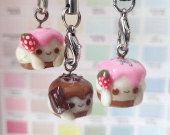 May include: Three miniature cake charms with pink and white frosting, chocolate frosting, and a strawberry on top. Each charm is attached to a silver chain.
