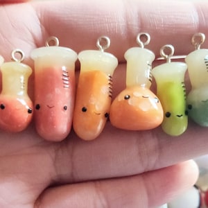 Op de afbeelding: Een verzameling van 10 kleurrijke, miniatuur glazen bekers met gouden toppen en schattige gezichtjes. De bekers zijn gevuld met verschillende gekleurde vloeistoffen en zijn perfect om een ​​whimsical touch toe te voegen aan elk project.