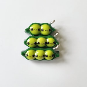 May include: Three green pea pod charms with cute faces, each with a silver loop for attaching to a necklace or bracelet.