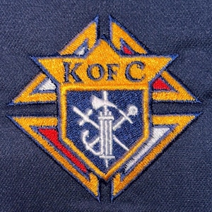 May include: Embroidered patch featuring the letters "K OF C" in gold on a navy blue background. The patch has a shield design with crossed swords, an anchor, and other symbols. The patch is surrounded by a gold and red border.