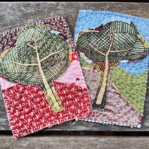 Może przedstawiać: Dwa ręcznie robione dzieła sztuki z tkaniny przedstawiające wyszywane drzewa z zielonymi liśćmi na kolorowym tle. Drzewa są wyszywane białą nicią, a tło wykonane jest z różnych tkanin.