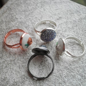 May include: Four rings with different coloured and patterned buttons. The rings are made of silver, copper, and black metal. The buttons are round and have a variety of designs.