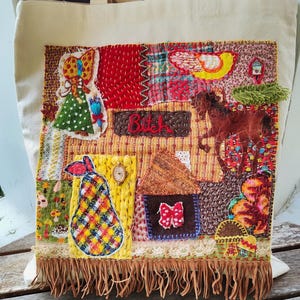 May include: Cream-colored tote bag with a patchwork design. The patchwork includes a girl, a pear, a house, and a horse. The word "Bitch" is embroidered on a brown rectangle. The bottom edge has a fringe.
