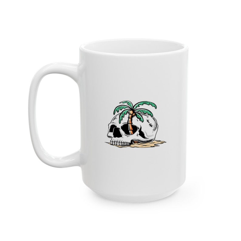 May include: White ceramic mug with a graphic of a skull with a palm tree growing out of the top of it. The skull is lying on its side on a sandy beach.