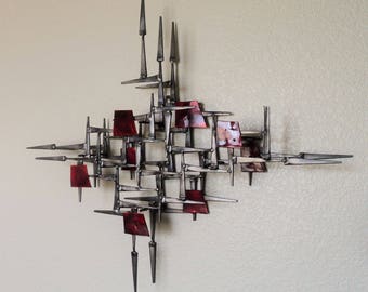 May include: A mid-century modern wall sculpture made of metal with red accents. The sculpture is abstract and geometric in design, with a variety of shapes and angles.