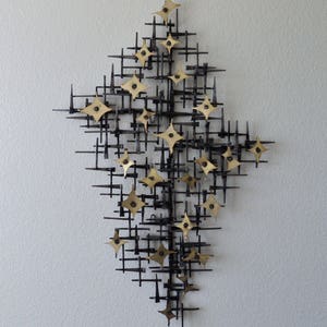 May include: A wall sculpture made of black metal with gold star-shaped accents. The sculpture is abstract and geometric in design.