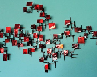 May include: A large, abstract wall sculpture made of metal and painted in shades of red. The sculpture is composed of many small squares connected by metal rods, creating a dynamic and textured surface.