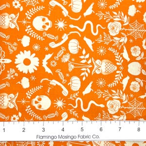 May include: Orange fabric with a repeating pattern of white Halloween-themed illustrations. The design includes skulls, pumpkins, owls, snakes, spiderwebs, flowers, and candy. The text "boo!" is printed on a telephone graphic.