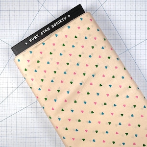 May include: A roll of fabric with a cream-colored background and a repeating pattern of small hearts in pink, green, and blue. The fabric is partially covered by a black label with the text "RUBY STAR SOCIETY".