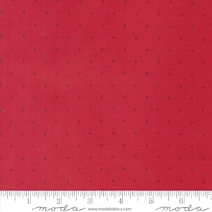 May include: Red fabric with a repeating pattern of small, dark brown dots. The fabric has a textured appearance and a ruler is visible along the bottom edge. The fabric is from Moda Fabrics.