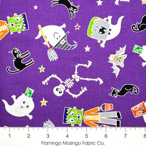 May include: Purple Halloween-themed fabric featuring cartoon illustrations of ghosts, cats, Frankenstein's monster, skeletons, bats, and stars. The fabric has a repeating pattern with a ruler at the bottom and the text "Flamingo Mosingo Fabric Co."