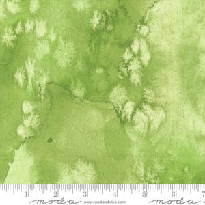 May include: Green fabric with a watercolor effect. The fabric features shades of green with lighter, textured areas, creating a mottled appearance. The fabric has a ruler along the bottom edge.