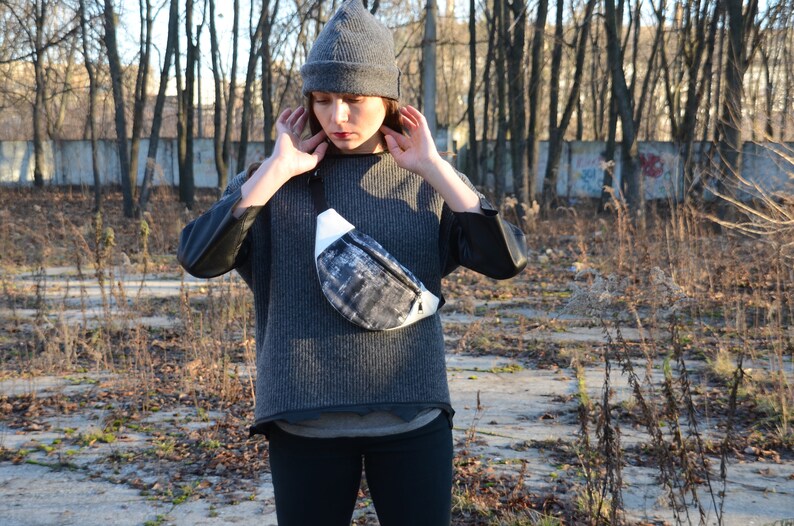 May include: A person wearing a gray beanie and a gray sweater with a black and white fanny pack.