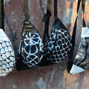 May include: Four black and white patterned fanny packs with adjustable straps. The fanny packs have different patterns, including a geometric pattern, a floral pattern, and a fish scale pattern.