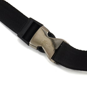 May include: Close-up of a black nylon strap with a silver metal buckle. The buckle is a simple, single-prong design.