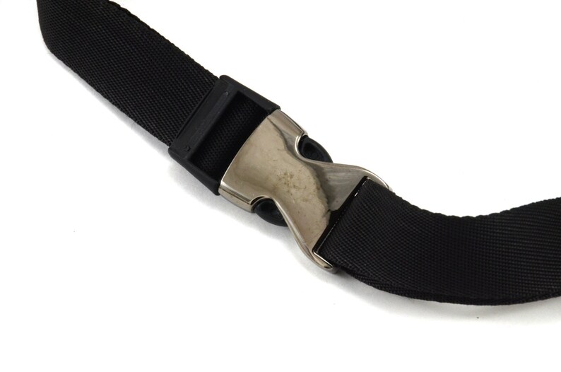May include: Close-up of a black nylon strap with a silver metal buckle. The buckle is a simple, single-prong design.