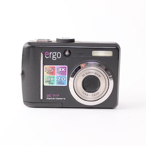 May include: A black Ergo DC 717 digital camera featuring a 3X super zoom lens, a 2.5 inch display, and 7.0 megapixels. The front of the camera displays the brand name Ergo, model number DC 717, and technical specifications printed on a sticker.