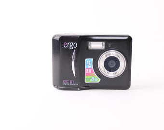 May include: A black digital camera with a silver lens and a silver button on the top. The camera has a screen on the back and the text "ergo" and "DC 91 Digital Camera" on the front. The camera has a sticker on the front that says "9 MP, 24x, 8x".
