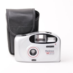 以下が含まれることがあります： 内蔵フラッシュと黒い革製のケースが付いた、銀色のハニメックス VC3200 35mm フィルムカメラです。