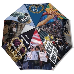 May include: A multi-paneled umbrella featuring various images and text. The umbrella's panels display images of crowds, protest signs, and a crown. Text includes phrases like "ICE OUT OF NEW YORK," "We've Already Had," and "The People."
