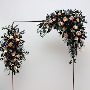 May include: A copper archway decorated with black and gold floral arrangements. The flowers are arranged in a cascading style, with black roses, gold orchids, and green foliage.