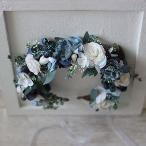 Pu&ograve; includere: Una corona floreale blu e bianca con fiori bianchi e foglie blu. La corona &egrave; realizzata con fiori di seta ed &egrave; perfetta per un matrimonio o un'altra occasione speciale.