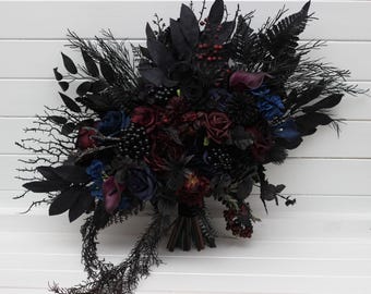 May include: A dark, gothic-style bouquet featuring a mix of black, burgundy, and blue flowers. The arrangement includes roses, berries, and various dark foliage, creating a dramatic and elegant floral display. The bouquet is set against a white background.