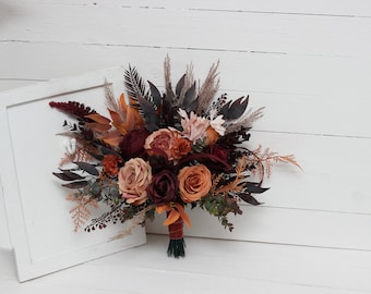 May include: A bouquet of faux flowers in shades of burgundy, orange, and brown. The bouquet includes roses, ferns, and dried grasses.