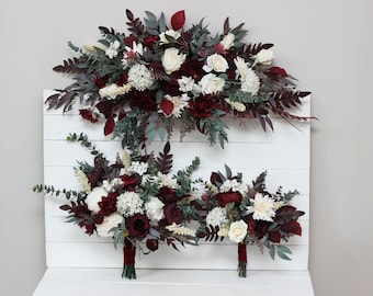 Op de afbeelding: Drie bordeauxrode en witte bloemboeketten met groen. De boeketten zijn gerangschikt op een witte houten achtergrond.