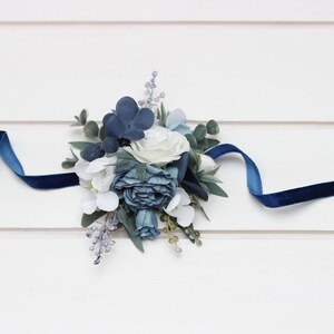 Pu&ograve; includere: Un braccialetto floreale blu e bianco con un nastro di velluto blu scuro.