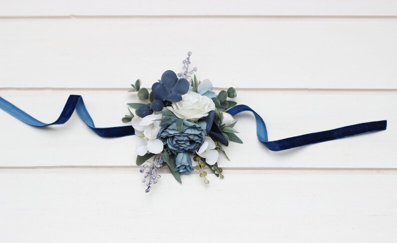 Pu&ograve; includere: Un braccialetto floreale blu e bianco con un nastro di velluto blu scuro.