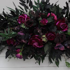 May include: A lush garland of deep purple and burgundy flowers with dark green leaves. The garland is perfect for adding a touch of elegance to any event.