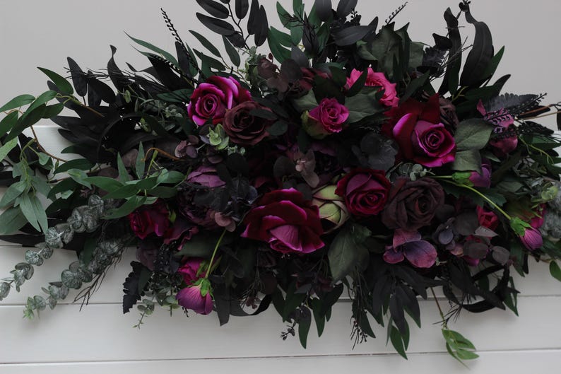 May include: A lush garland of deep purple and burgundy flowers with dark green leaves. The garland is perfect for adding a touch of elegance to any event.